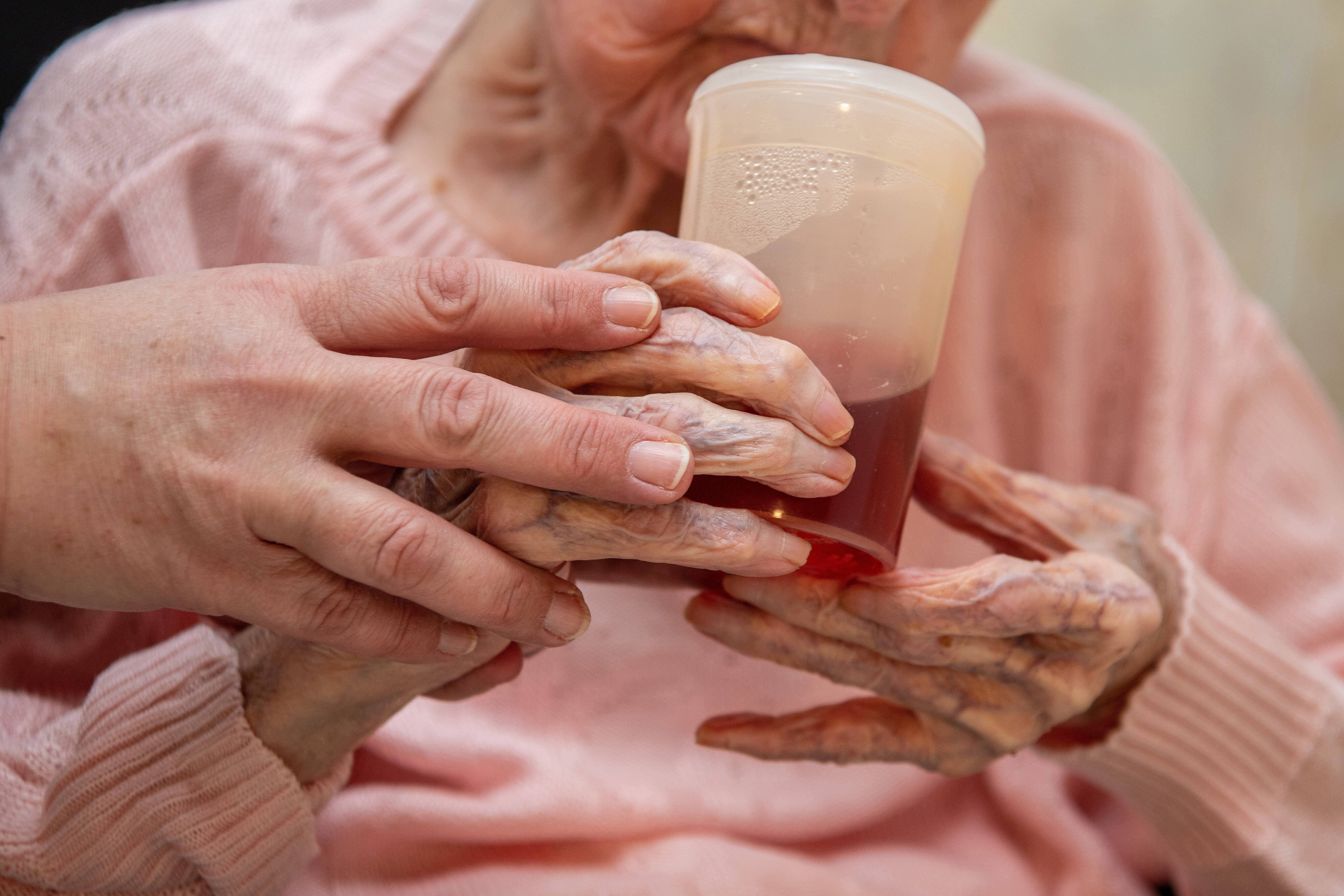 Seniorin im Pflegeheim Eine Altenpflegerin hilft einer Seniorin beim Halten eines Trinkbechers.