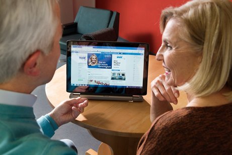Ein &auml;lteres Paar am Computer, auf dem Bildschirm sieht man die Facebook-Seite des VdK Deutschland