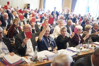 Die Delegierten heben ihre roten Stimmkarten zur Abstimmung.