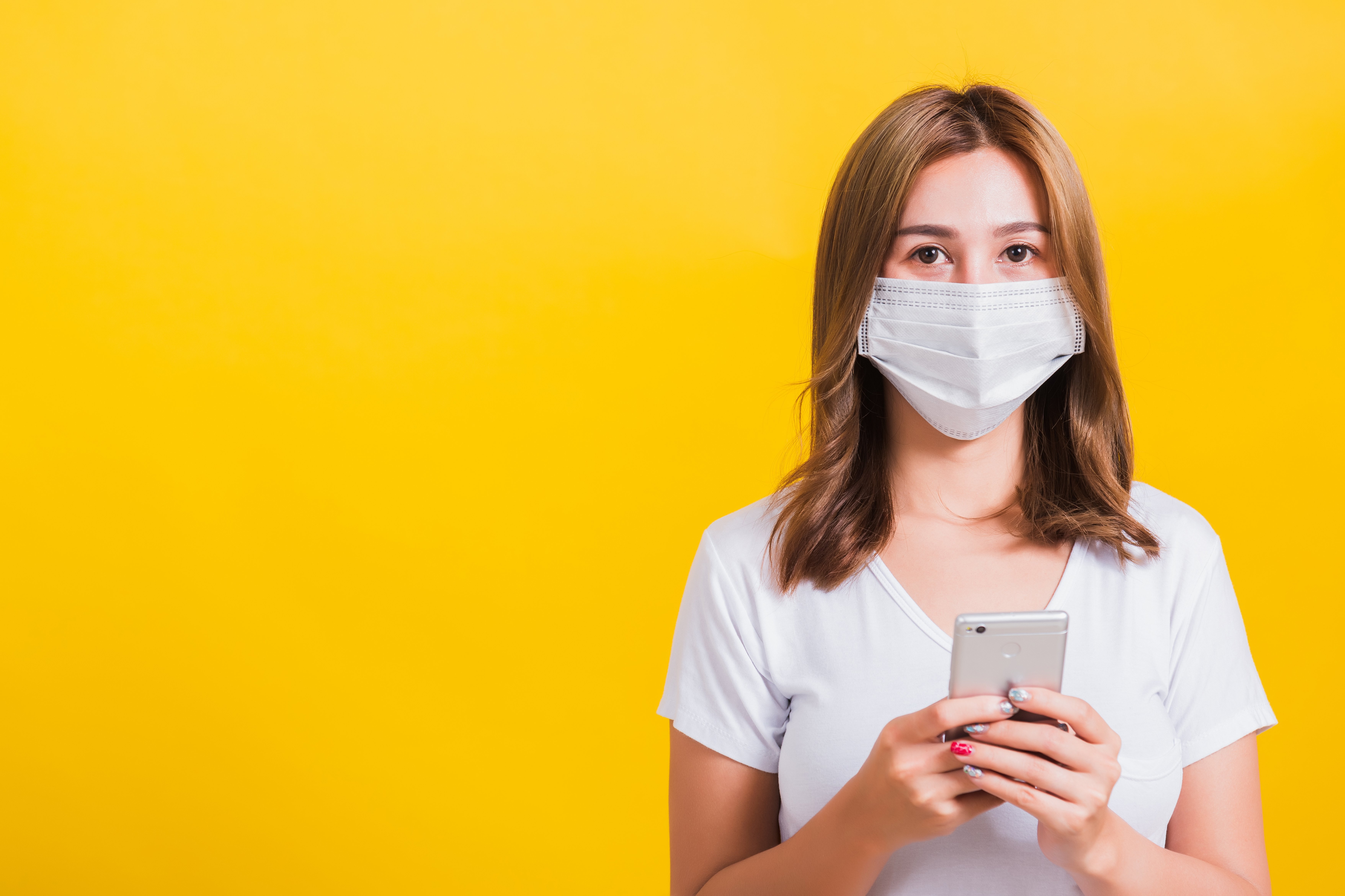 Eine junge Frau, die einen Mundschutz trägt, hält ein Smartphone in der Hand.