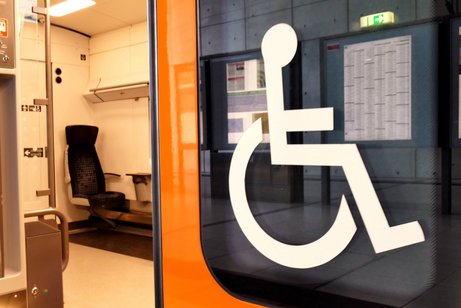 Blick in einen Bahnwaggon einer Regionalbahn mit einem Sitzplatz für Fahrgäste im Rollstuhl. Außen an der Fensterscheibe ist ein großes Rollstuhl-Symbol.