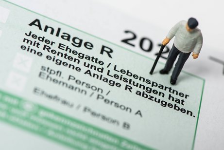 Ein kleines Rentner-Figürchen steht auf einer Papier-Steuererklärung mit der Anlage R für Renten