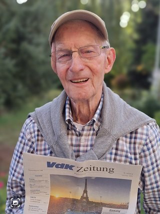 Ein Mann mit Mütze und Brille hält die VdK-Zeitung in der Hand.