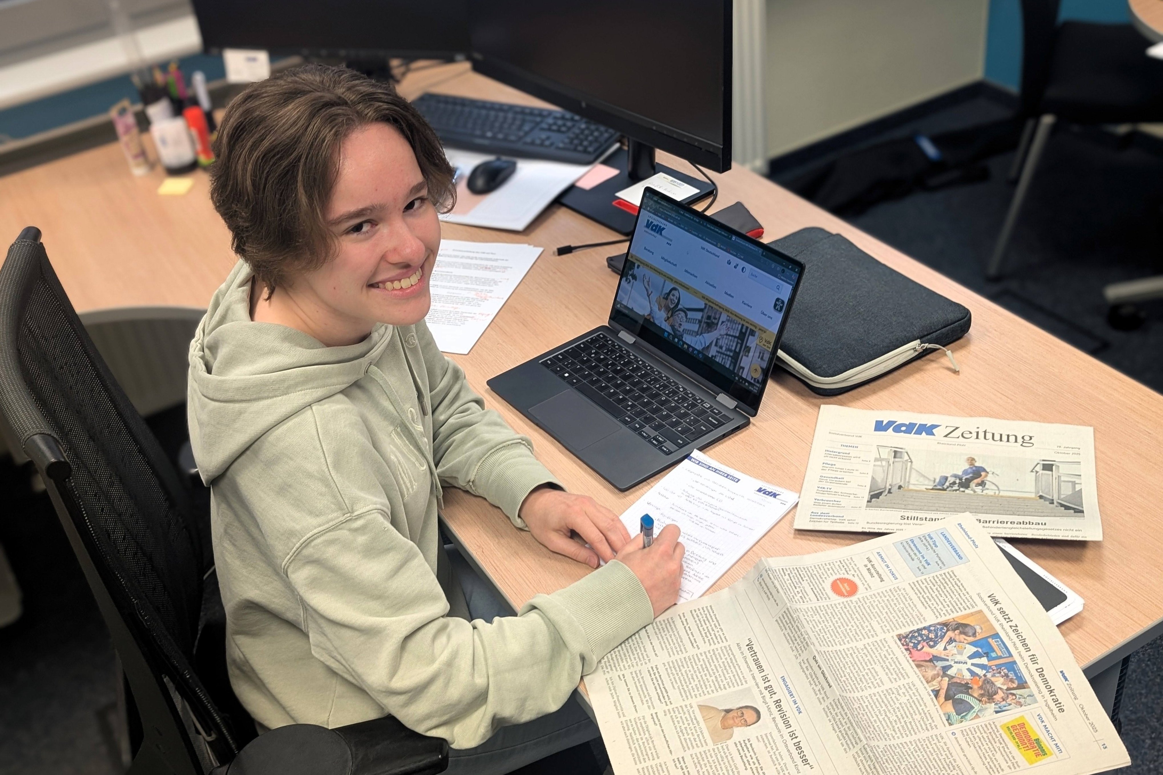 Eine junge Frau sitzt an einem Schreibtisch vor einem Laptop und einer aufgeschlagenen Zeitung.