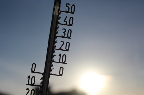 Ein Thermometer vor blauem Himmel mit Sonne.