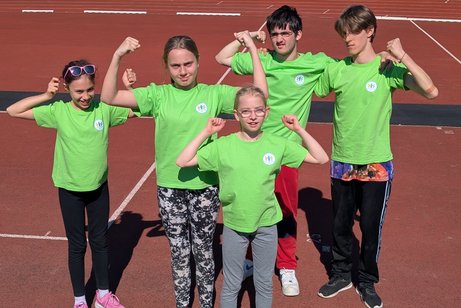 Fünf Mädchen und Junge in grünen T-Shirts zeigen ihre Muskeln.