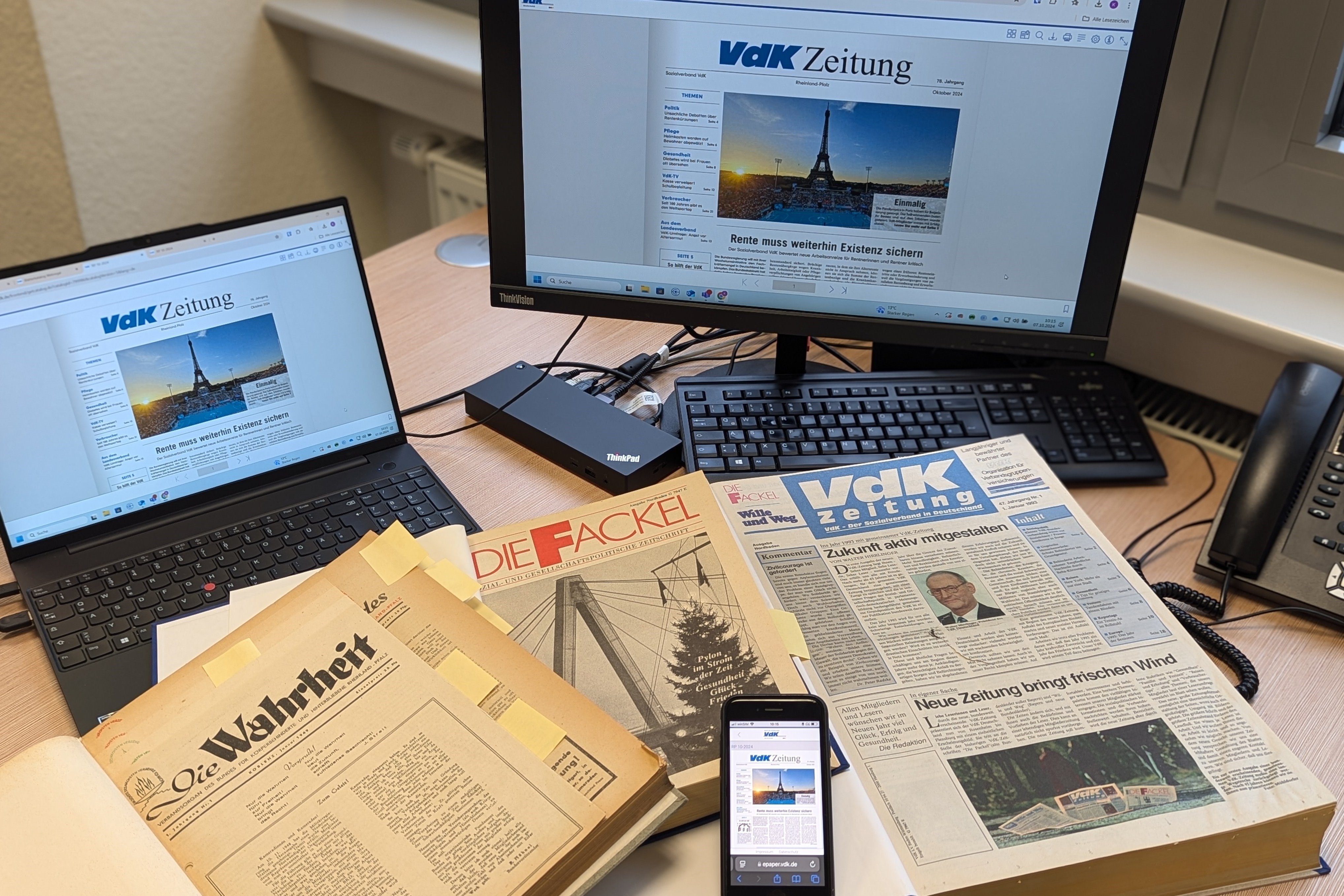 Auf einem Tisch sind verschiedene Medien wie eine Zeitung, Bücher, ein PC und ein Handy zu sehen.