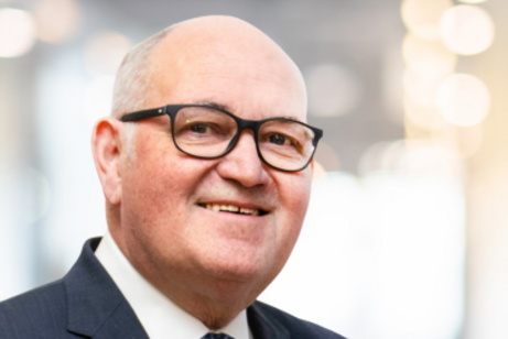 Porträtbild von einem Mann. Er trägt eine Brille und einen Anzug.