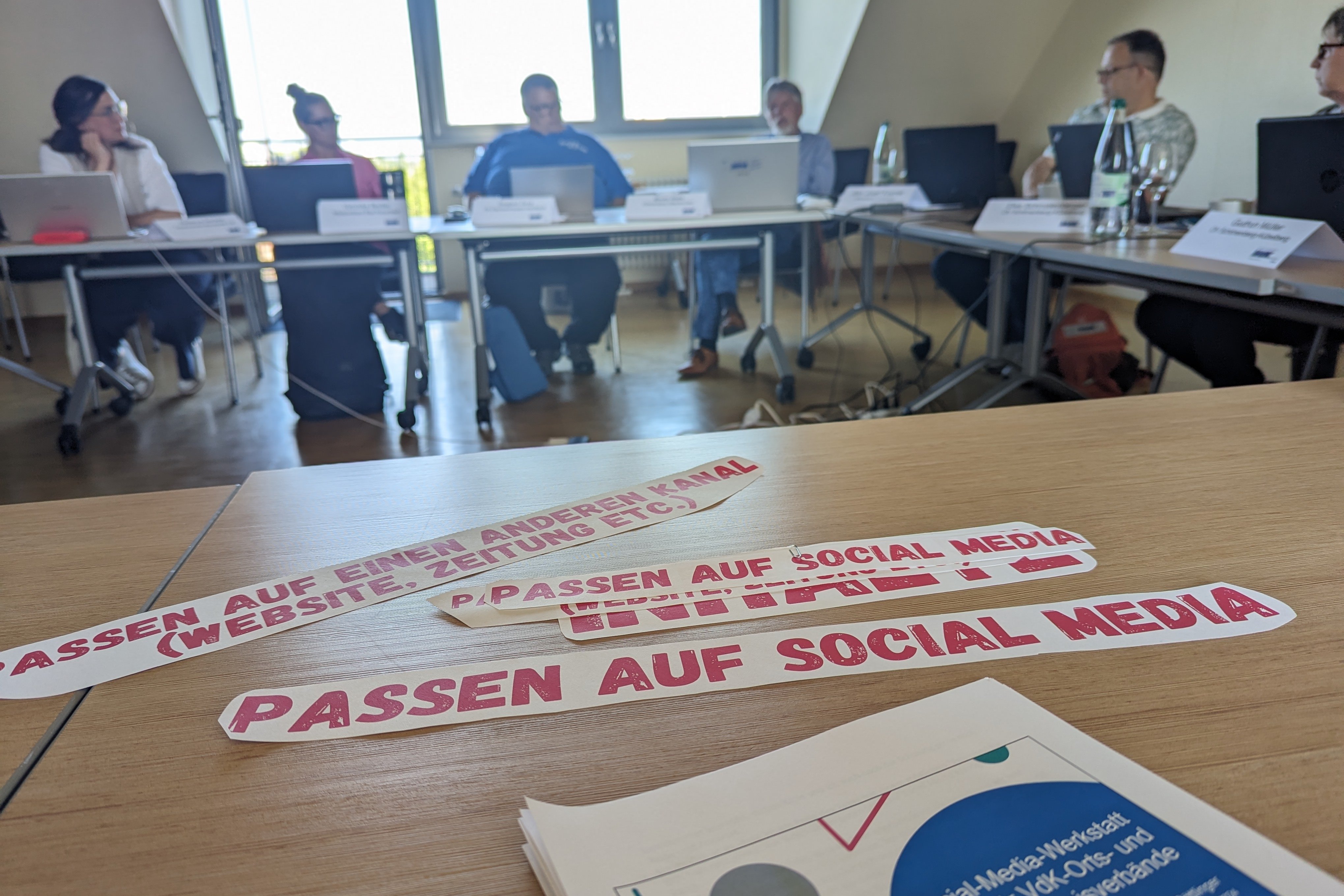 Auf einem Tisch liegen Stichwortzettel zu Social-Media-Themen. Im Hintergrund sitzen die Teilnehmenden.