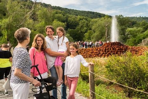 Eine &auml;ltere Dame mit Rollator steht mit Kindern und Enkeln vor dem Geysir.
