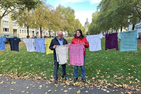 Ein mann und eine Frau stehen vor einer Wäscheleine mit T-Shirts und halten je eins in der Hand