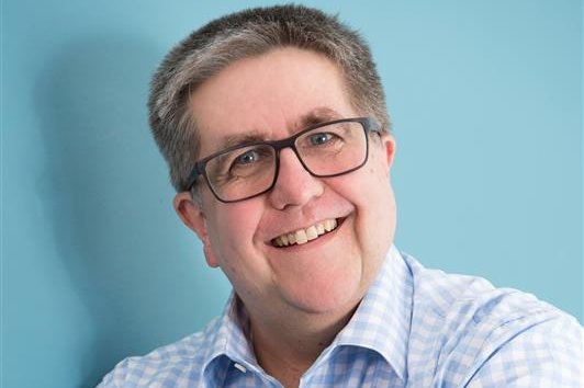 Porträtbild eines Mannes mit Brille. Er trägt ein karriertes Hemd.