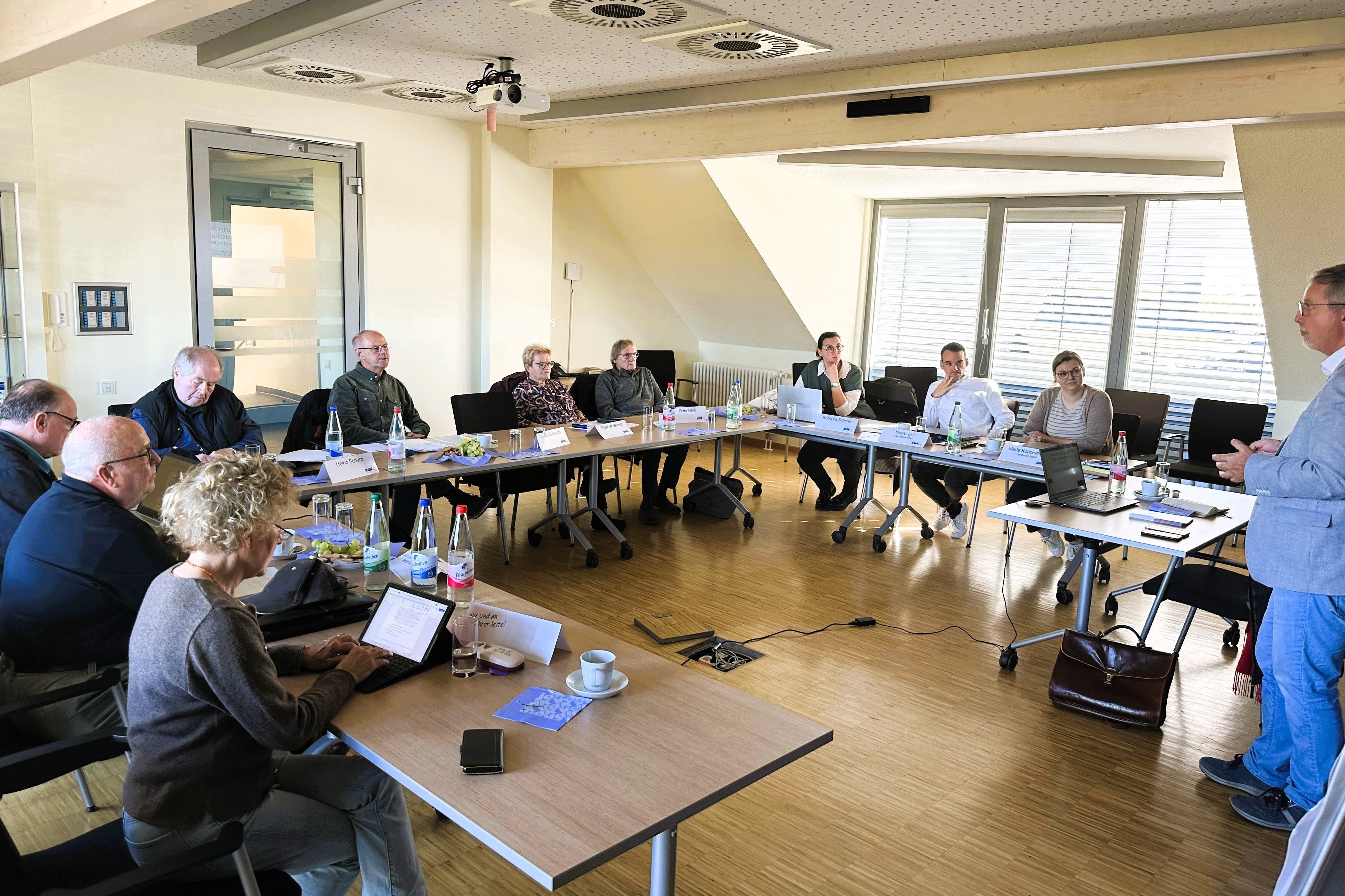 Frauen und Männer sitzen an Tischen in einem Tagungsraum.