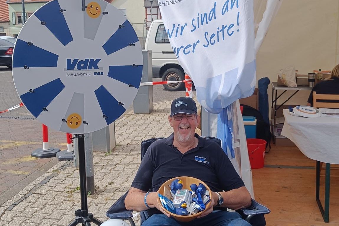 Ein Mann sitzt vor einem Glücksrad mit dem VdK-Logo.