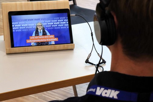 Eine person mit Kopfhörern sitzt vor einem Tablet.