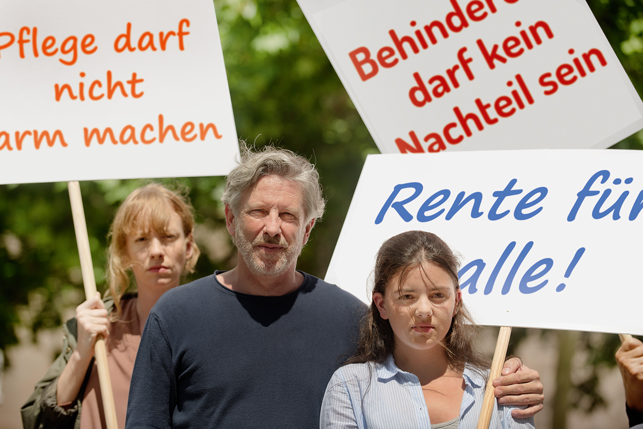 Demo für soziale Gerechtigkeit Gruppe von Menschen verschiedenen Geschlechts und Alters, mit und ohne Behinderung, demonstrieren. Auf den Demopappen steht "Pflege darf nicht arm machen", "Behinderung darf kein Nachteil sein" und "Rente für alle"