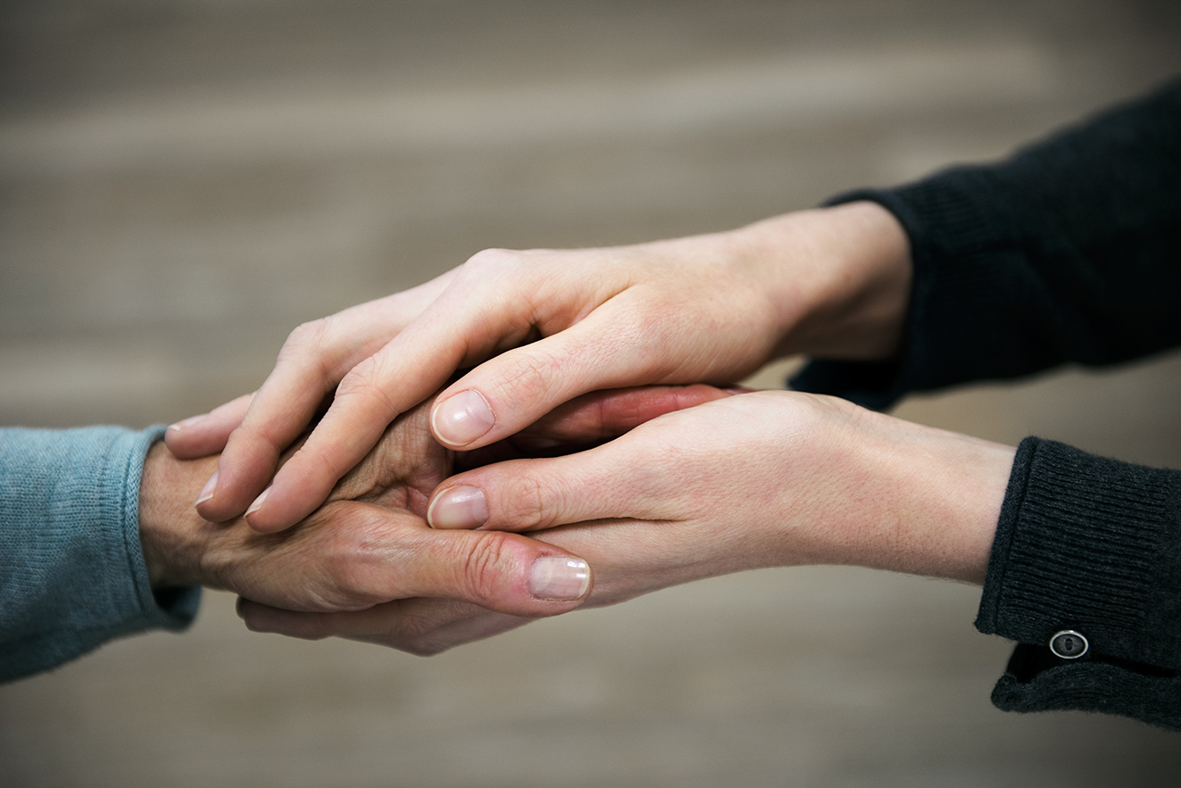Handhalten als tröstende Geste Die Hand einer jüngeren Frau hält die Hand einer älteren Frau in einer tröstenden Geste.