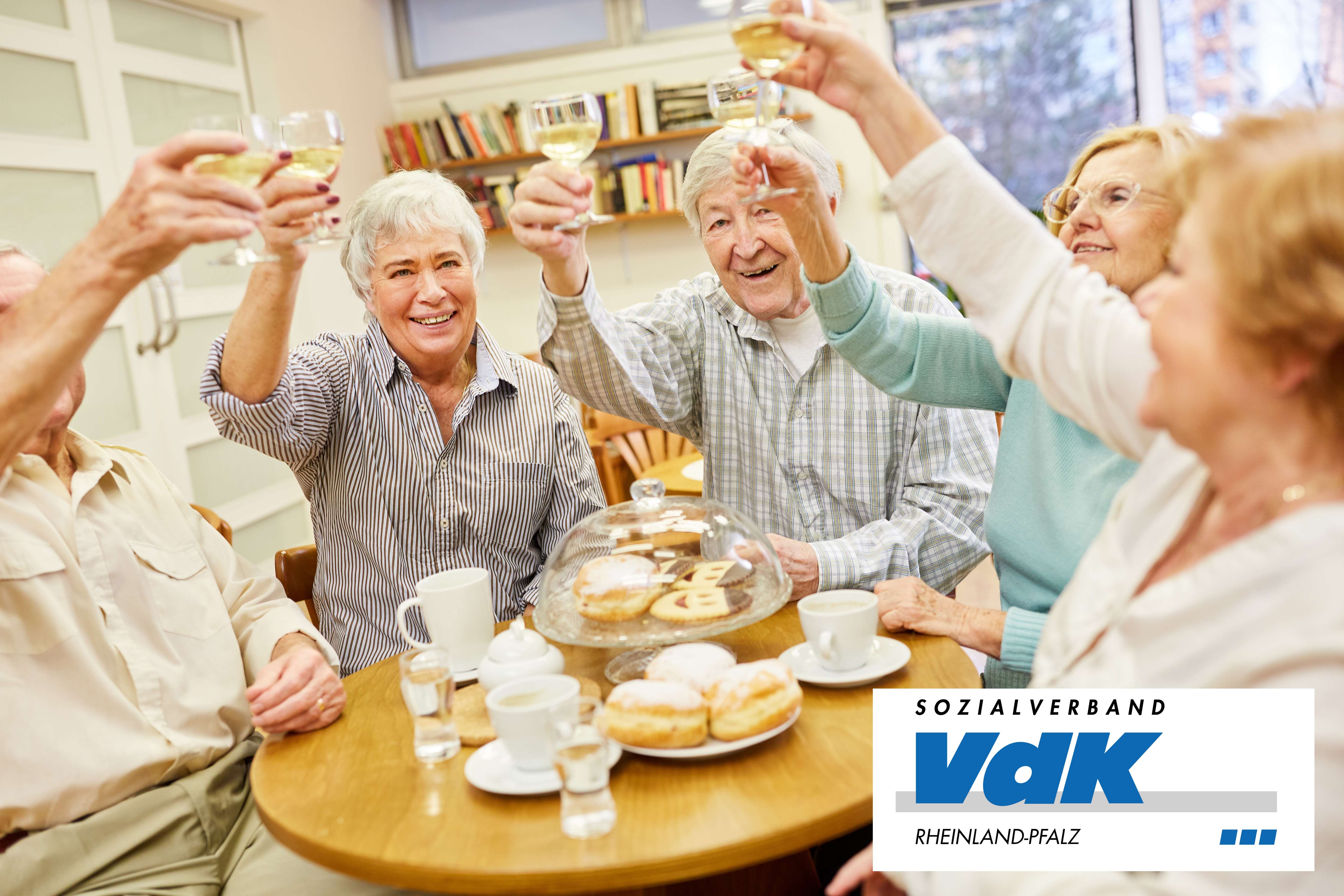 &Auml;ltere Menschen sto&szlig;en gemeinsam an einem gedeckten Tisch mit Gl&auml;sern an.