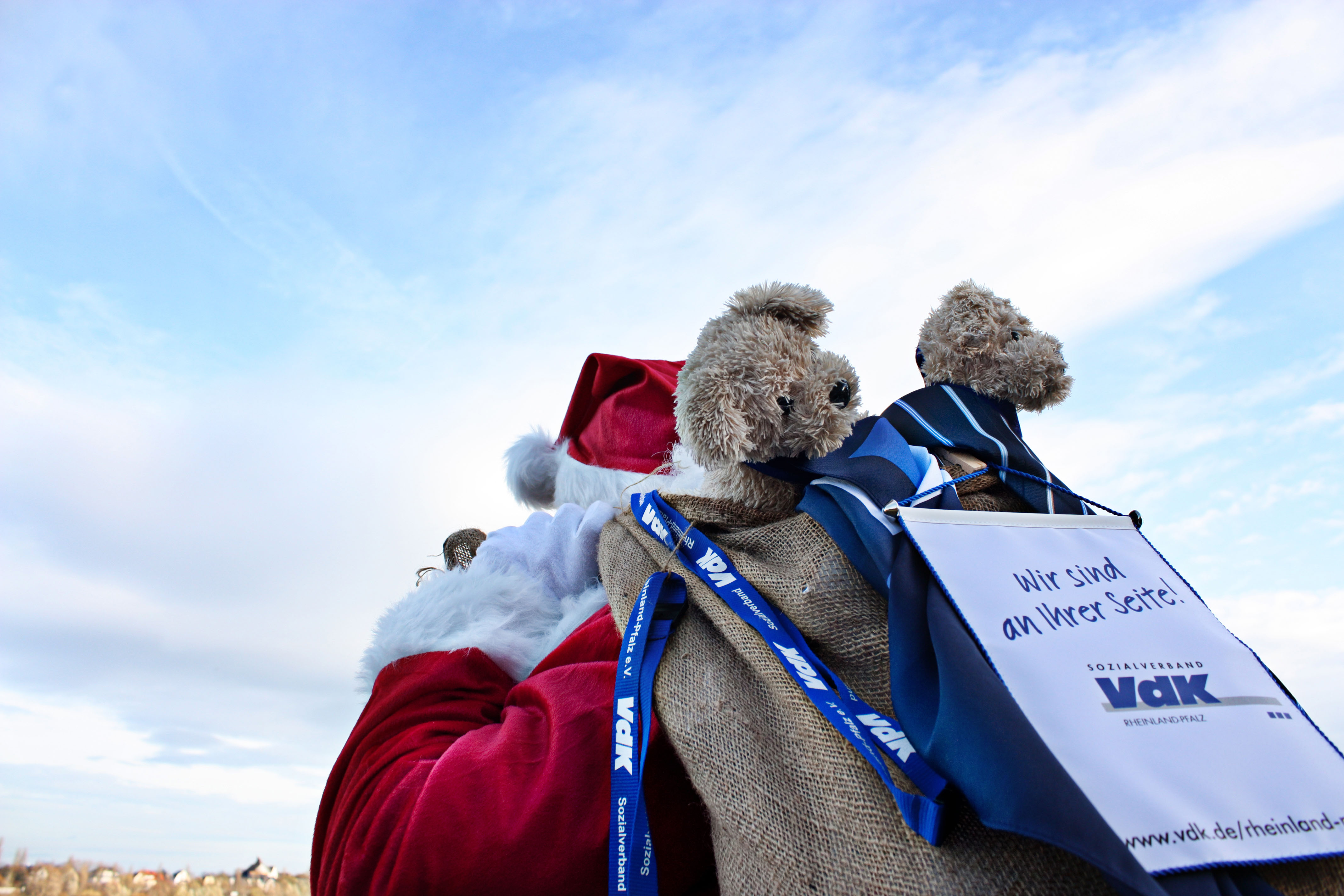 Ein Weihnachtsmann mit einem Jutesack auf dem R&uuml;cken aus dem der VdK-Hund "Viktor" schaut.