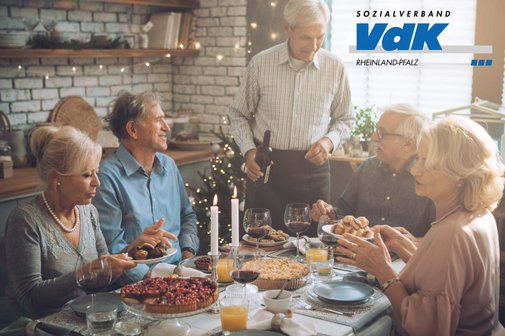 Frauen und Männer sitzen an einem weihnachtlich gedeckten Tisch und unterhalten sich.