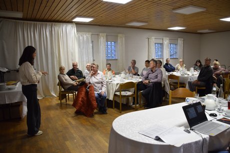 Frau Rapp im Vordergrunde, vor Zuh&ouml;renden an zwei runden Tischen