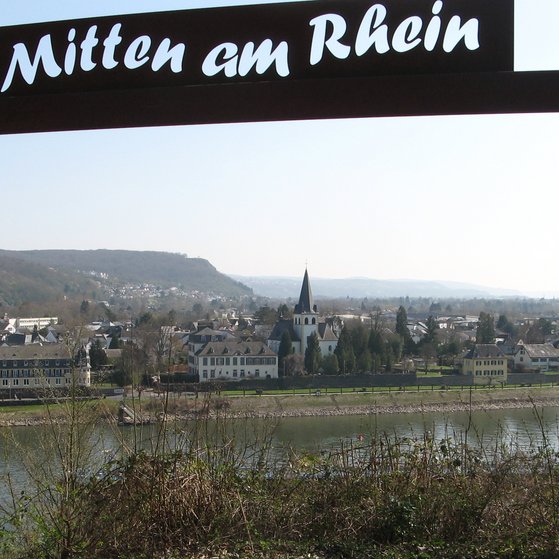 Ein Bilderrahmen mit der Aufschrift "Mitten am Rhein" und im Rahmen liegt das St&auml;dtchen mit dem Rhein davor
