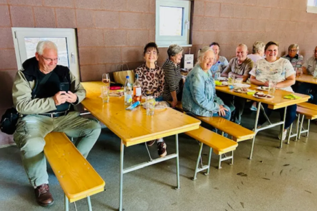 Menschen sitzen auf Bierbänken in einem großen Raum.