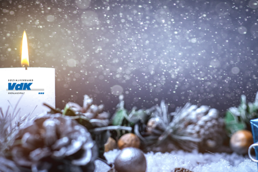 Kerze mit VdK-Logo und Weihnachtsdekoration.