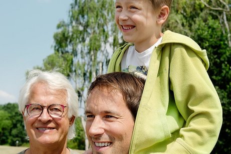 Männer aus drei Generationen Drei Männer - ein älterer Mann lächelt in die Kamera, ein jüngerer Mann blickt in die Ferne, auf seinen Schultern sitzt ein Junge.