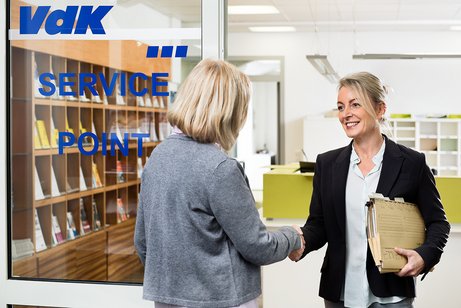 Eine VdK-Mitarbeiterin begr&uuml;&szlig;t eine Frau an der T&uuml;r einer VdK-Beratungsstelle. Sie hat eine Aktenmappe unter dem Arm. 