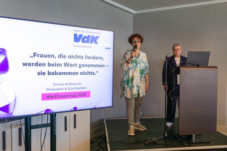Elisabeth Dobias und Siegrun Breutigam stehen auf dem Podium neben einem VdK-Banner und begrüßen die Teilnehmerinnen.