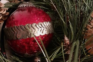 Dunkelrote Weihnachtskugel eingebettet in Kiefernnadeln, an der Seite sind Kiefernzapfen und Strohsterne