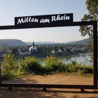 Ein Bilderrahmen mit der Aufschrift "Mitten am Rhein" und im Rahmen liegt das Städtchen mit dem Rhein davor