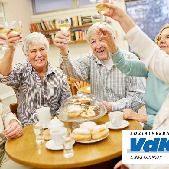 &Auml;ltere Menschen sto&szlig;en gemeinsam an einem gedeckten Tisch mit Gl&auml;sern an.