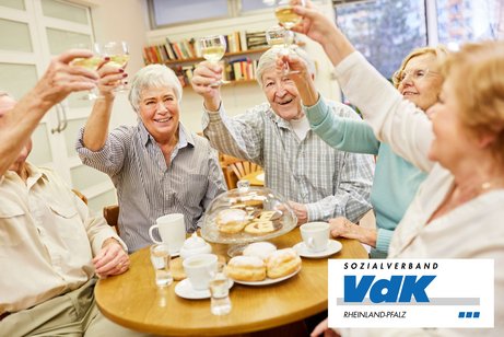 &Auml;ltere Menschen sto&szlig;en gemeinsam an einem gedeckten Tisch mit Gl&auml;sern an.