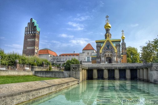 Bild der Mathildenhöhe. Wasserbecken im Vordergrund, Kirche und Turm im Hintergrund
