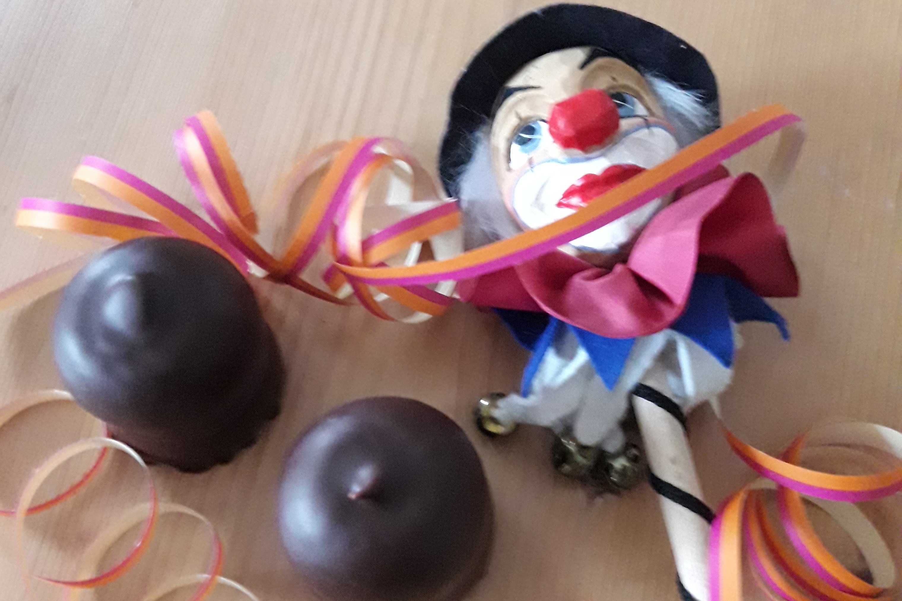 Neben 2 Schaumküssen liegt ein Stabclown mit Schellen. Das ganze ist mit Luftschlangen umgeben.