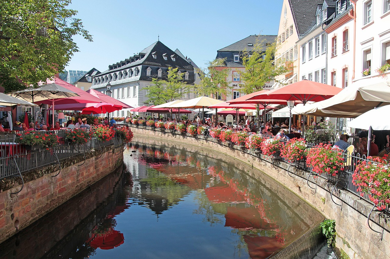 Saarburg Innenstadtbereich von Saarburg am blumengeschmückten Ufer der Saar mit Tischen unter Sonnenschirmen