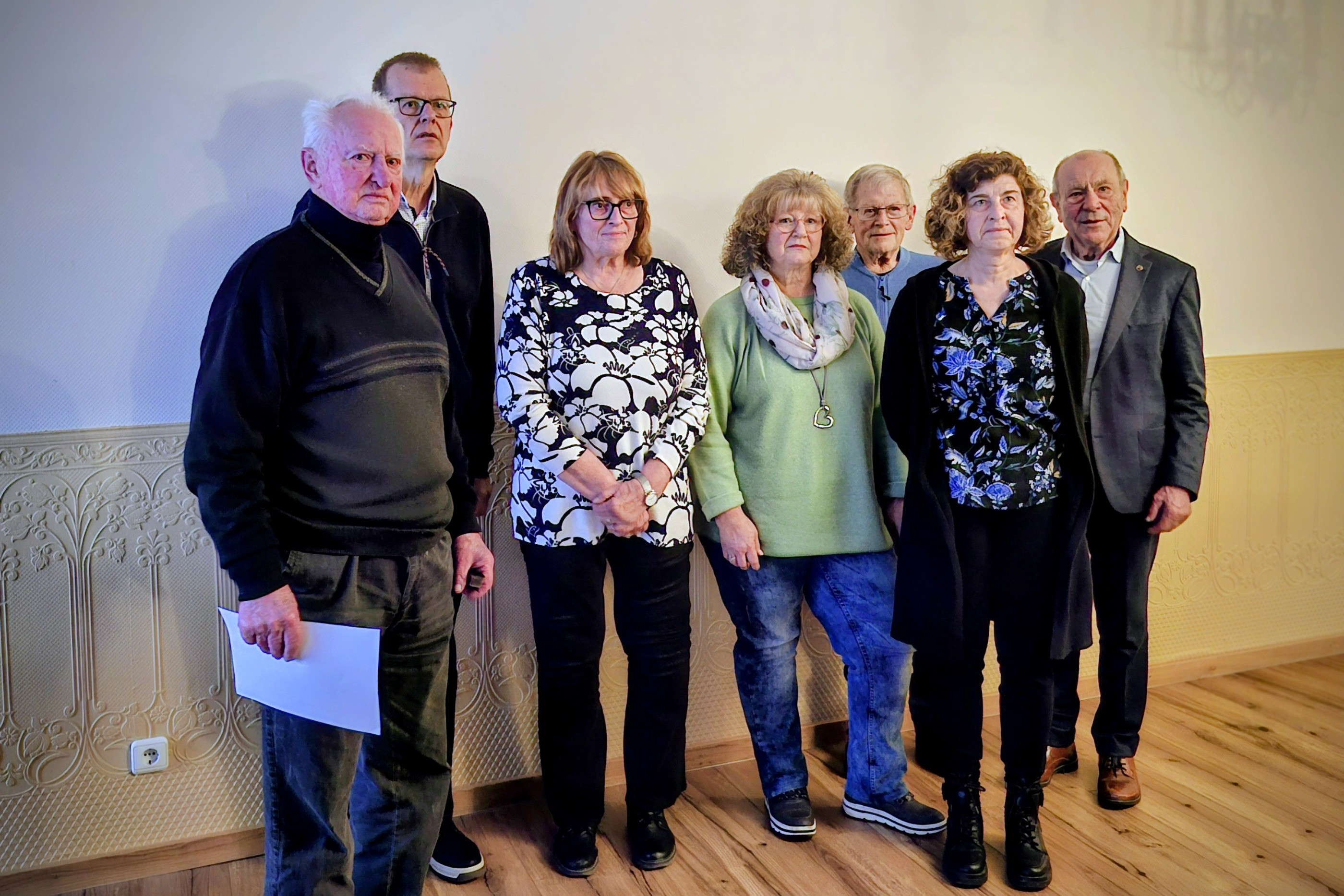 verschiedene Menschen stehen vor einer Wand und halten Urkunden in den H&auml;nden.