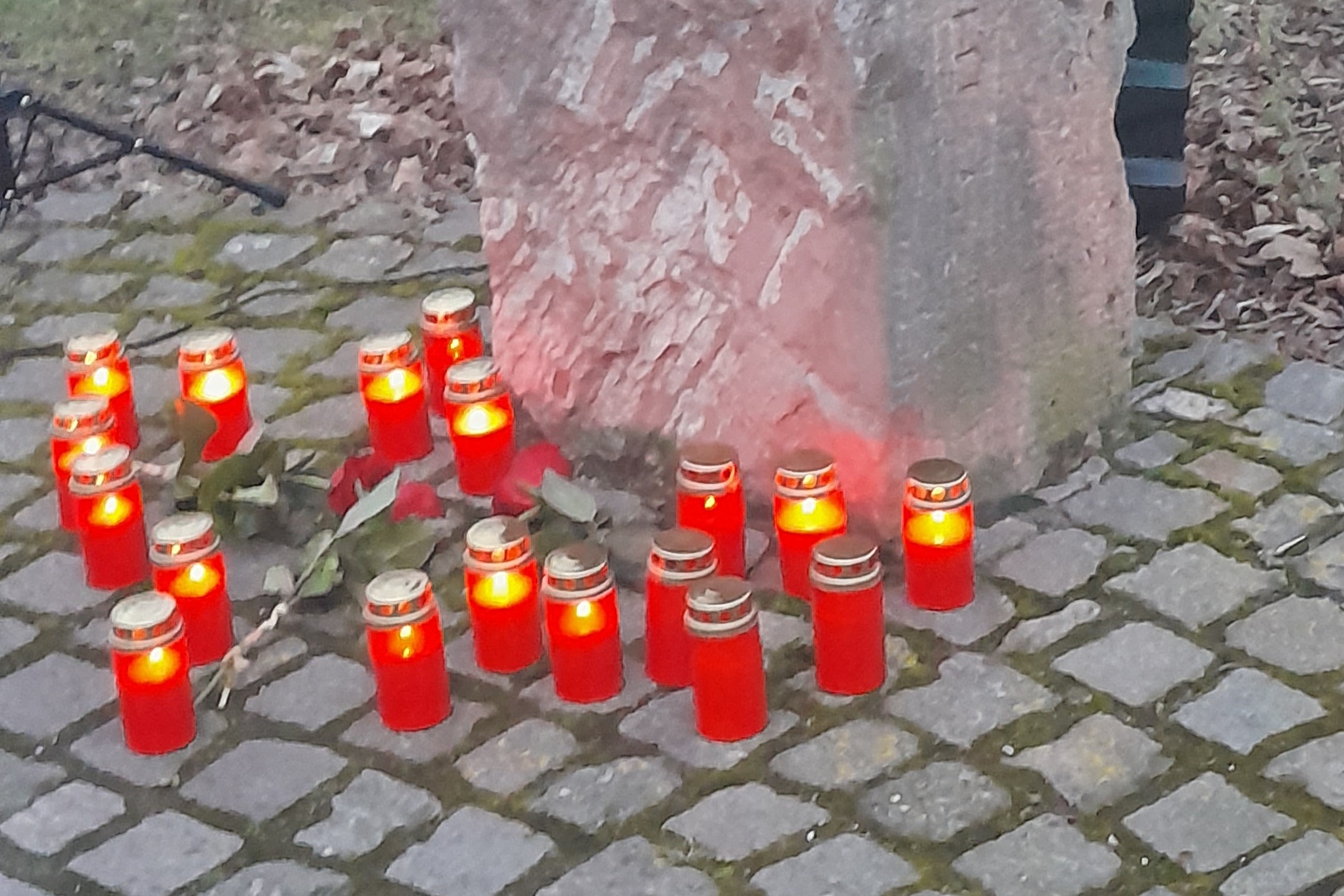 Am Gedenkfindling stehen entzündete Kerzen und liegen rote Rosen.