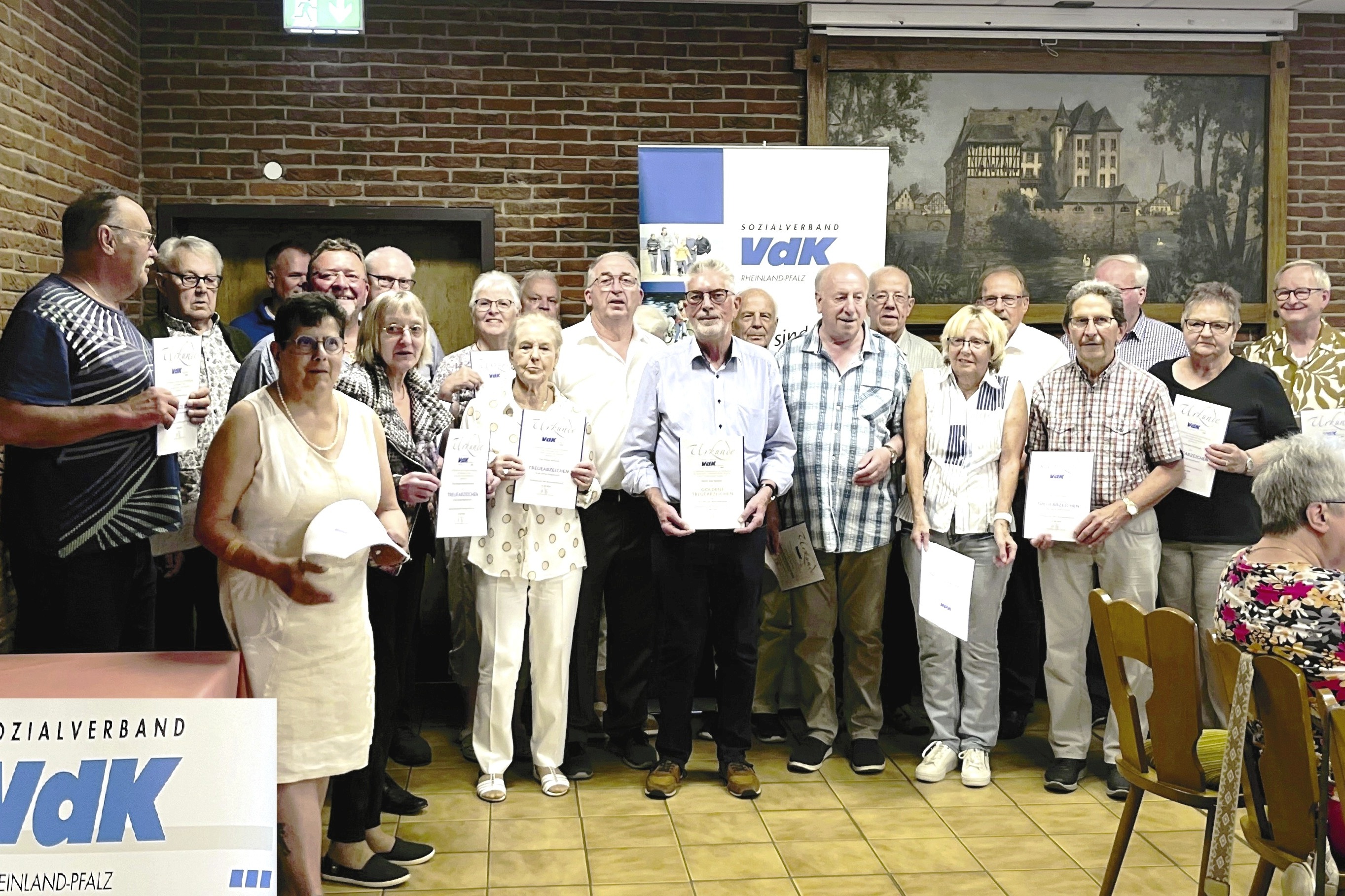 Gruppenbild der Geehrten In einem Halbkreis haben sich die Geehrten vor einer VdK Tafel aufgestellt und zeigen Ihre Urkunden